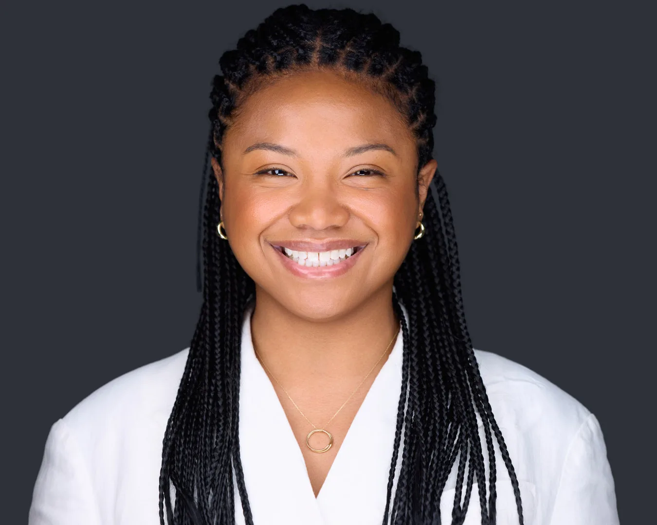 Professional headshot of a smiling woman in a white blazer and gold hoop earrings