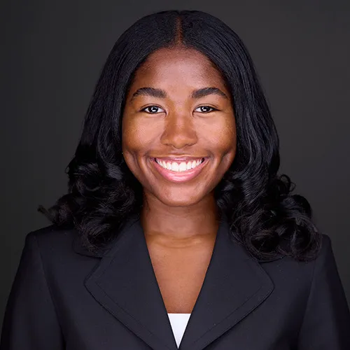 Taylor Leonard professional law firm headshot in navy blazer with bright smile and long dark hair against neutral gray studio backdrop