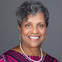 Nancy professional headshot with confident smile in purple patterned top against gray studio background, client testimonial for headshot photography