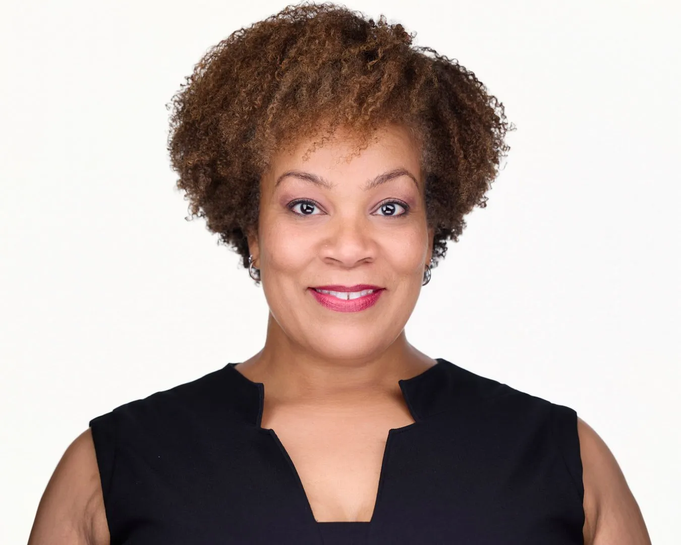 Professional headshot of woman with curly brown hair and bright smile wearing black sleeveless top
