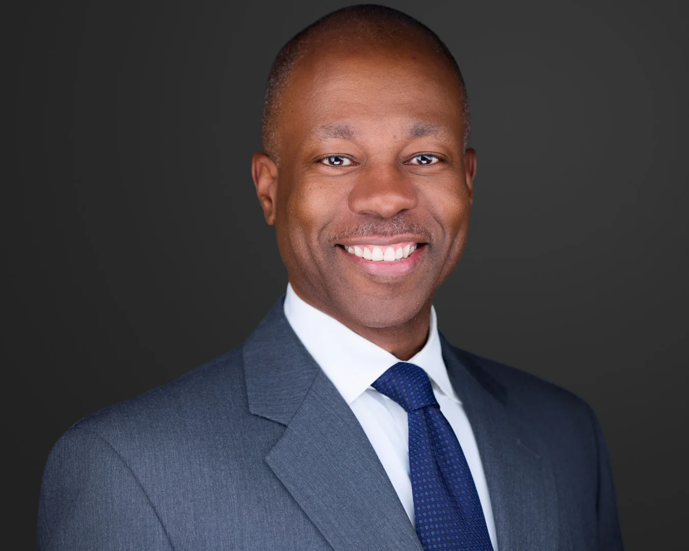 Professional headshot of a businessman in a gray suit and navy tie