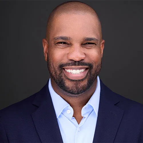 Chris Willis corporate headshot in navy blazer and light blue shirt with confident smile and well-groomed beard against charcoal gray background