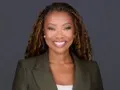 C. Everett professional headshot in olive blazer with dreadlocked hair against neutral gray backdrop